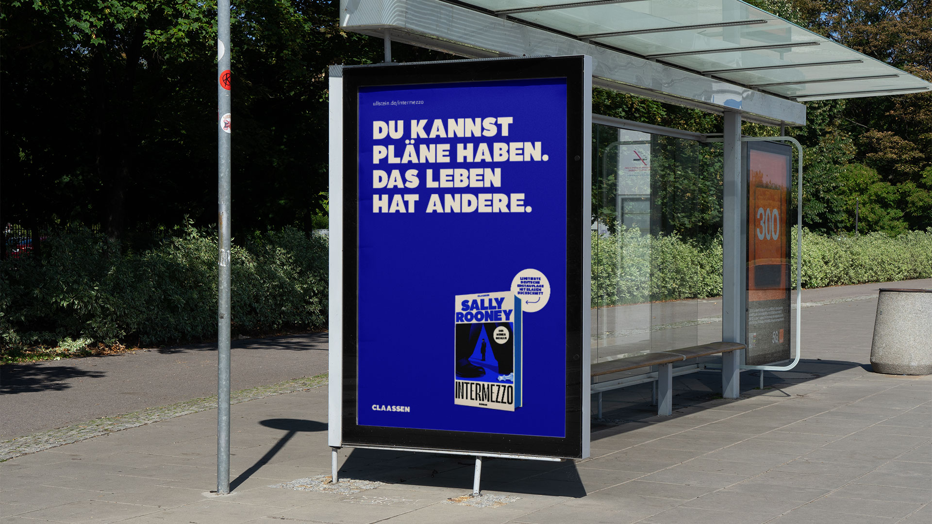 City Light Poster für „Intermezzo“ von Sally Rooney an einer Bushaltestelle mit der Headline „Du kannst Pläne haben. Das Leben hat andere“ in Blau und dem Buchcover, gestaltet von THIS IS JUJU.